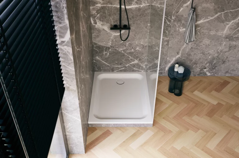 Weiße Duschwanne in moderner Dusche mit grauer Marmoroptik, Glasabtrennung, schwarzer Armatur und hellem Fischgrätboden.