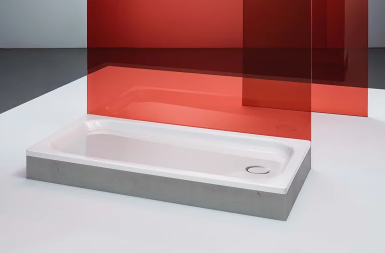 Rechteckige Duschwanne aus Stahl-Email mit abgeflachten Kanten, seitlich rotes Glaspaneel im Hintergrund.