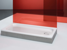 Rechteckige Duschwanne aus Stahl-Email mit abgeflachten Kanten, seitlich rotes Glaspaneel im Hintergrund.