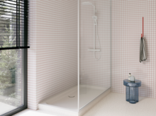 Weiße Duschwanne in einer hellen, bodengleichen Dusche mit weißen Mosaikfliesen, Glasabtrennung und großem Fenster.