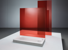 Rechteckige Duschwanne aus Stahl-Email mit flacher Form, daneben rote Glasabtrennung, modernes minimalistisches Design.