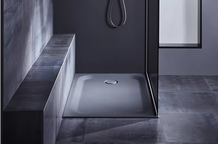 Rectangular steel enamel shower tray with central drain, installed flush with the floor, surrounded by dark tiles and bench.