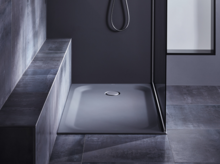 Rectangular steel enamel shower tray with central drain, installed flush with the floor, surrounded by dark tiles and bench.