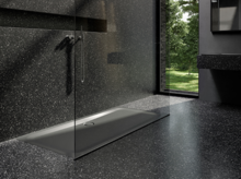 Rectangular steel enamel shower tray, flush with floor, modern bathroom with dark stone floor and glass partition.