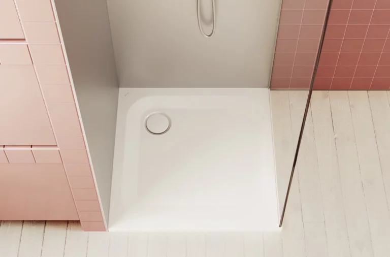 Weiße, quadratische Duschwanne mit Wandarmatur, umgeben von rosa Fliesen und hellem Holzboden.