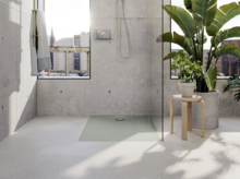 Piatto doccia rettangolare in acciaio smaltato, a filo pavimento, in bagno moderno con parete in cemento e grandi piante.