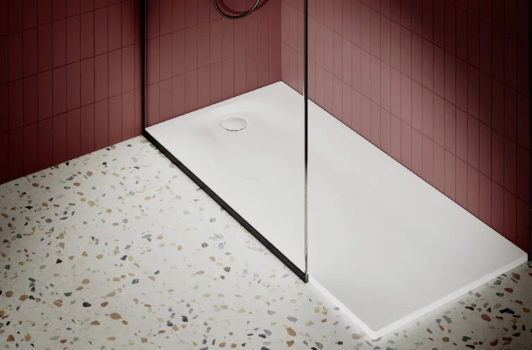 Piatto doccia rettangolare in acciaio smaltato con scarico centrale, accanto a pavimento decorato e piastrella rossa a parete.