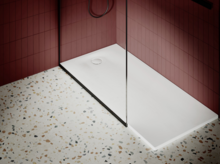 Piatto doccia rettangolare in acciaio smaltato con scarico centrale, accanto a pavimento decorato e piastrella rossa a parete.