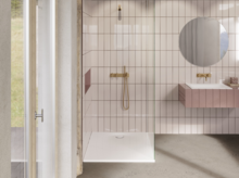 Helles Bad mit bodengleicher Dusche, vertikalen Fliesen, goldener Armatur, rundem Spiegel und schwebendem Waschtisch.