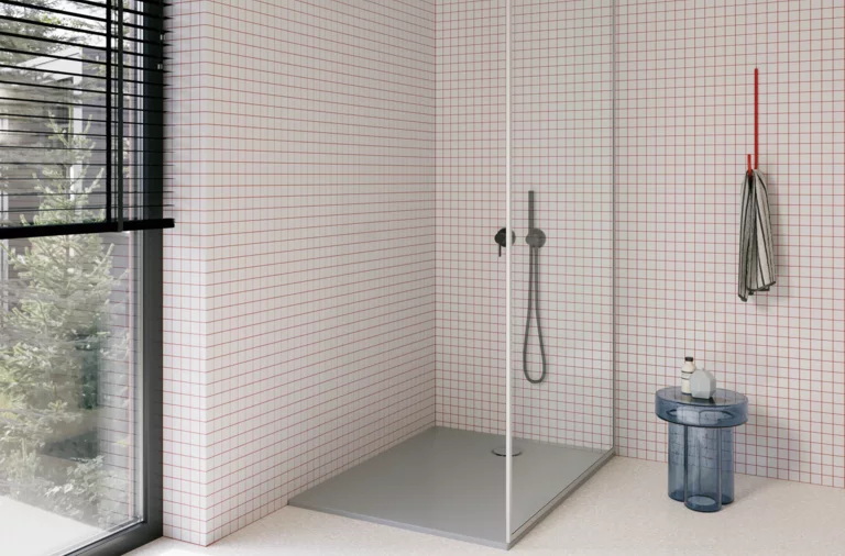 Moderne Dusche mit grauer bodengleicher Duschwanne, Glasabtrennung, dunkler Armatur und kleinteilig weiß gefliesten Wänden.