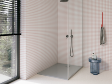 Moderne Dusche mit grauer bodengleicher Duschwanne, Glasabtrennung, dunkler Armatur und kleinteilig weiß gefliesten Wänden.