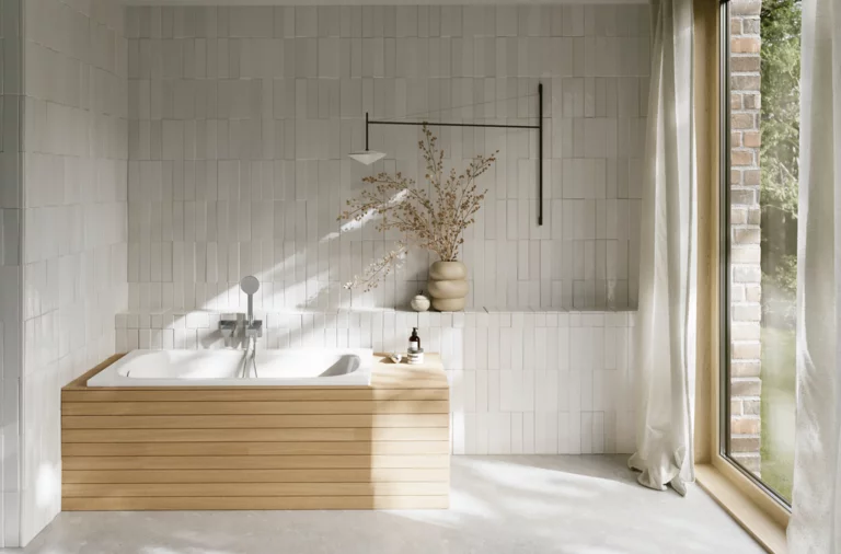 Helles Bad mit eingebauter Badewanne, heller Verkleidung, Fliesenwand, bodentiefem Fenster und Vorhang.