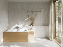 Helles Bad mit eingebauter Badewanne, heller Verkleidung, Fliesenwand, bodentiefem Fenster und Vorhang.