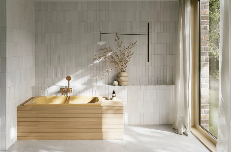Helles Bad mit goldfarbener eingelassener Badewanne, heller Front, Fliesenwand, großem Fenster und Vorhang.
