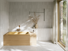 Helles Bad mit goldfarbener eingelassener Badewanne, heller Front, Fliesenwand, großem Fenster und Vorhang.