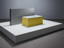Rectangular steel-enamel bathtub with yellow cladding, on white pedestal in modern room.