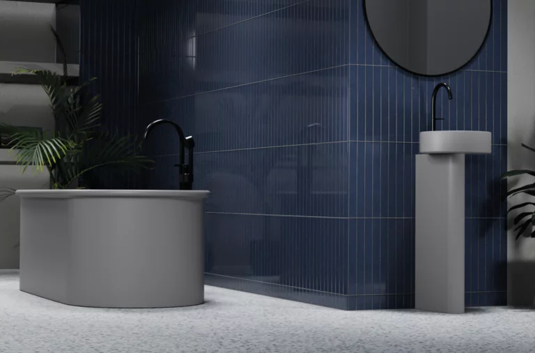 Freestanding steel-enamel bathtub, oval, next to round pedestal basin in front of blue tiles.