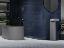 Freestanding steel-enamel bathtub, oval, next to round pedestal basin in front of blue tiles.