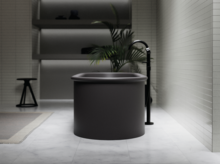 Freestanding round steel-enamel bathtub in dark color, modern bathroom with freestanding faucet.