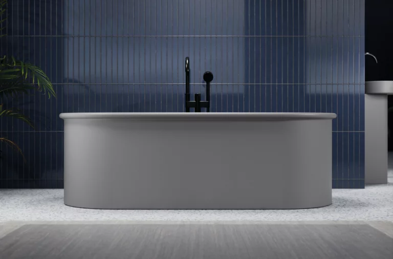 Freestanding oval steel-enamel bathtub in front of blue tiled wall, central faucet, bright bathroom.
