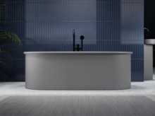 Freestanding oval steel-enamel bathtub in front of blue tiled wall, central faucet, bright bathroom.