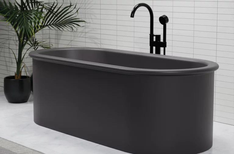 Freestanding oval bathtub made of steel enamel in dark grey, with black fittings in front of white wall.