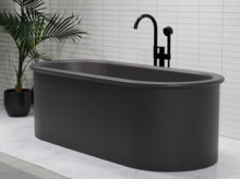 Freestanding oval bathtub made of steel enamel in dark grey, with black fittings in front of white wall.