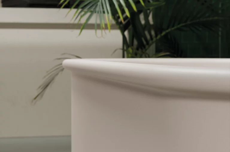 Round steel-enamel bathtub in foreground, plants and washbasin with countertop in background.