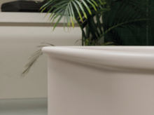 Round steel-enamel bathtub in foreground, plants and washbasin with countertop in background.