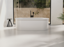 Freestanding oval steel-enamel bathtub in front of large windows in minimalist bathroom.