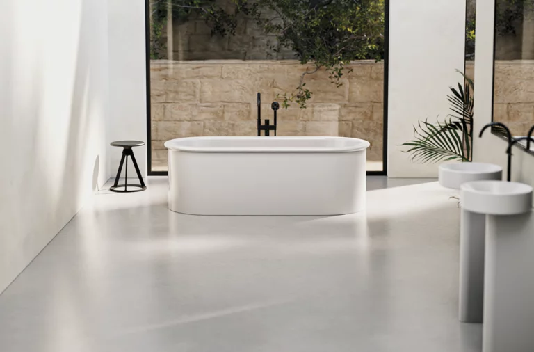 Freestanding oval bathtub made of steel enamel in modern bathroom with washbasin and countertop, bright surroundings.